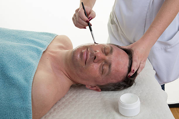 Spa therapy for man receiving facial mask at beauty salon.