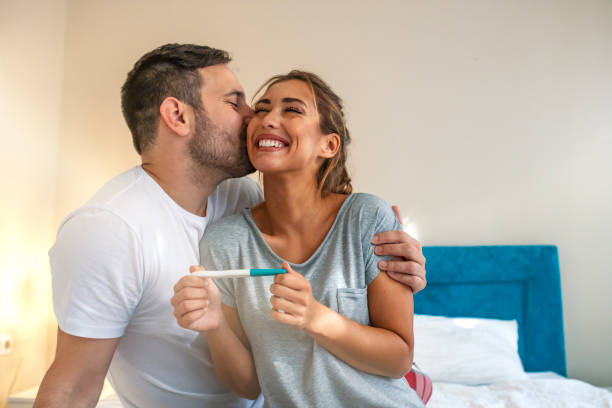 Young couple is happy because of positive pregnancy test. Affectionate couple finding out results of a pregnancy test in their bedroom. Family, parenting and medical concept